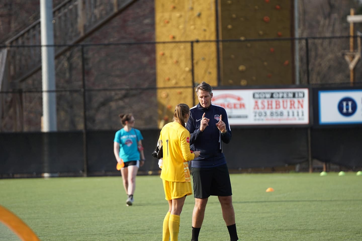 Tréner inštruuje mladú futbalistku na umelom trávniku.
